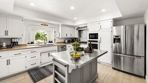 Uma cozinha moderna com armários brancos, eletrodomésticos de aço inoxidável e uma ilha central com frutas.