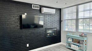 A modern living room with a black brick wall, a flat-screen TV, a fireplace, and a window with blinds. - Beach apartment, Recently Renovated, With Balcony (Clearwater)