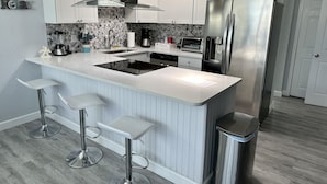 A modern kitchen with white cabinets, a stainless steel refrigerator, a built-in oven, and a central island with bar stools. - Beach apartment, Recently Renovated, With Balcony (Clearwater)