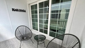 A room with a large window, two black wire-framed chairs, a small round table, and a sign on the wall reading "BEACH TOWELS". - Beach apartment, Recently Renovated, With Balcony (Clearwater)