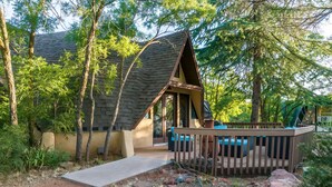 A rustic cabin with a sloped roof, a porch with blue cushions, and a wooden deck. - Beautiful Unique home with yoga/meditation studio! (Sedona)