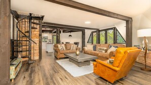 A spacious living area with a staircase, wooden flooring, and a mix of furniture including a sofa, armchair, and coffee table. - Beautiful Unique home with yoga/meditation studio! (Sedona)