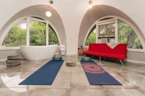 Un'ampia stanza con una grande vasca da bagno, un divano rosso e tappetini da yoga sul pavimento.