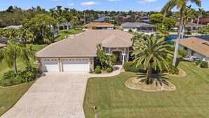 A residential house with a garage, a swimming pool, and a well-maintained lawn. - Pet friendly sailboat access property w/4BRs! Great for families! Villa Andrea - SWFL Rentals (Cape Coral)