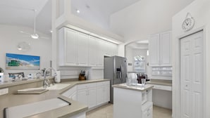 A modern kitchen with white cabinets, a central island, a refrigerator, and a clock on the wall. - Pet friendly sailboat access property w/4BRs! Great for families! Villa Andrea - SWFL Rentals (Cape Coral)