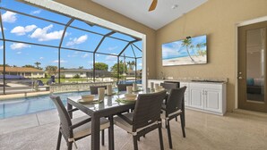 A dining area with a view of a swimming pool, a ceiling fan, and a kitchen with white cabinets. - Pet friendly sailboat access property w/4BRs! Great for families! Villa Andrea - SWFL Rentals (Cape Coral)