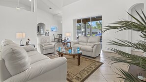 A spacious living room with a high ceiling, a glass coffee table, and two beige sofas. - Pet friendly sailboat access property w/4BRs! Great for families! Villa Andrea - SWFL Rentals (Cape Coral)