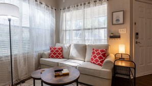 A living room with a beige sofa, two red patterned pillows, a wooden coffee table, and a floor lamp.