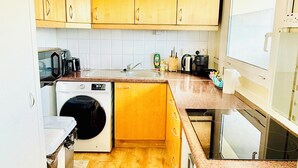 A compact kitchen with wooden cabinets, a washing machine, a coffee maker, and a window.