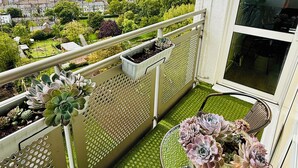 A balcony with a view of a cityscape, a small table with flowers, and potted plants.