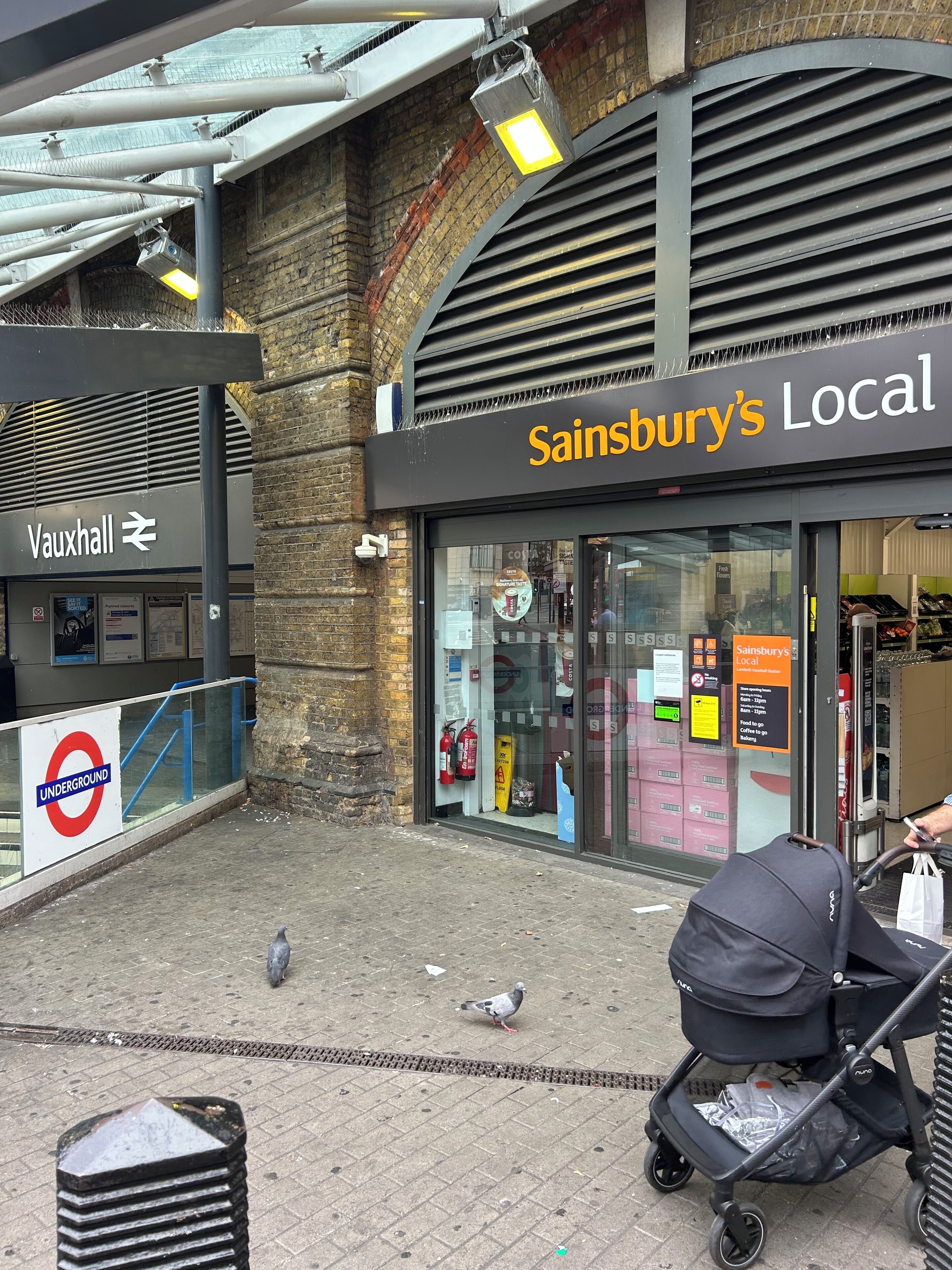 A storefront with a sign for 'Sainsbury's Local' and an adjacent 'Vauxhall' sign.