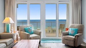 A room with a view of the ocean, featuring two armchairs, a small table, and a lamp.