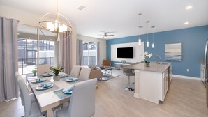 A modern kitchen with a central island, a dining area with a table set for four, and a living area with a sofa and TV. - LN4816 Storey Lake Home 4Beds 3Baths Private Pool and Free Waterpark (Kissimmee)