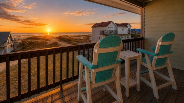A wooden deck with two green Adirondack chairs and a small table, overlooking a beach and a house. - Calypso's Dream (North) | Oceanfront | Hot Tub and Dog Friendly (Nags Head)