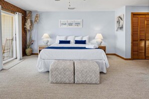 Un dormitorio con una cama, dos mesitas de noche, una ventana con cortinas, una puerta y una pared decorada con tres cuadros.