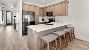 A modern kitchen with wooden cabinets, stainless steel appliances, a large island with bar stools, and a tiled backsplash. - 12 The Vues | Resort pool, Private balcony, (Saint George)