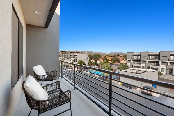 Un balcon avec des fauteuils en osier et une vue sur une piscine et des immeubles.