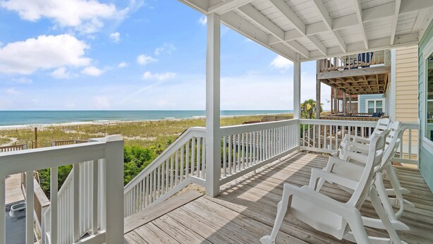 Une terrasse en bois avec des balustrades blanches donnant sur une plage.