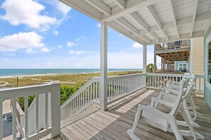 Une terrasse en bois avec des balustrades blanches donnant sur une plage.