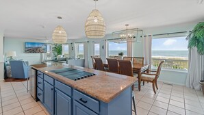 Une cuisine moderne dotée d’un grand îlot central, d’un coin repas avec des chaises et d’une vue sur l’océan.