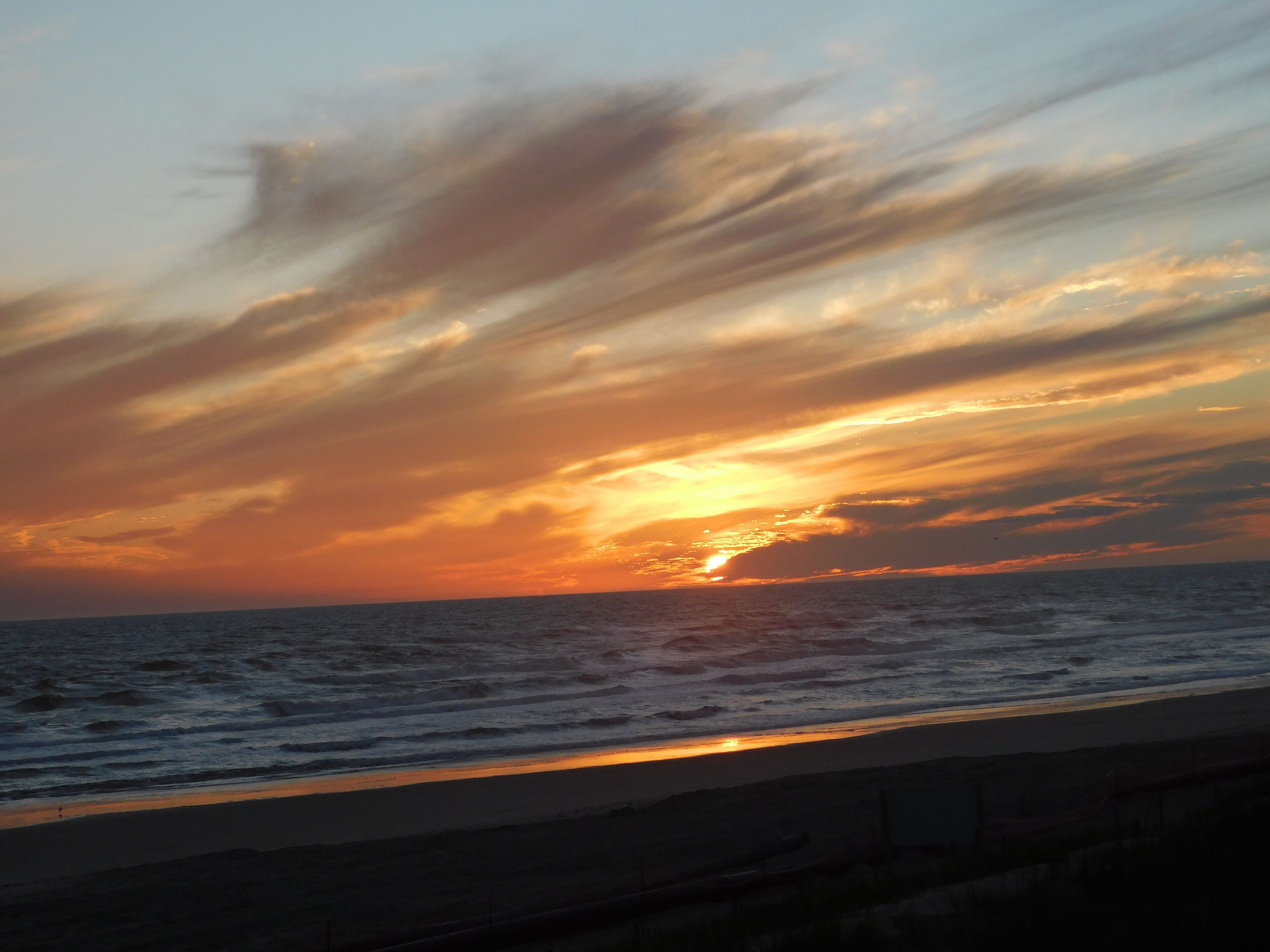Un atardecer sobre el océano, con una playa en primer plano.