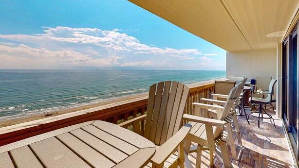 Un balcon avec vue sur l’océan, des chaises en bois et une table.