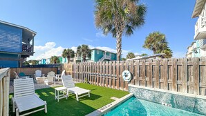 A backyard with a swimming pool, wooden fence, and lounge chairs.