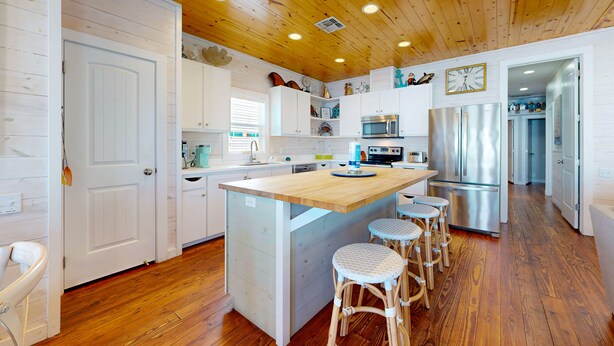 A modern kitchen with white cabinetry, wooden flooring, and a central island with bar stools.