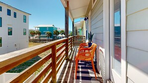 A balcony with wooden railings, two orange chairs, and a view of neighboring buildings.