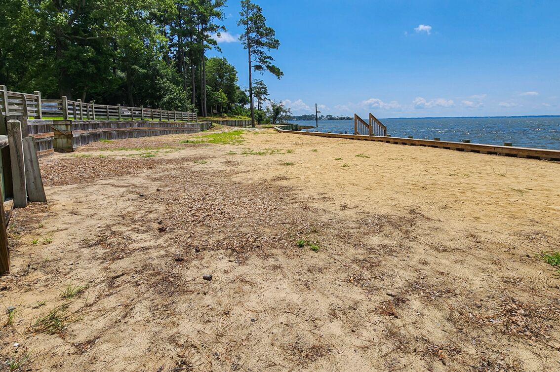 A sandy beach area with a wooden fence and a wooden walkway leading to the water.