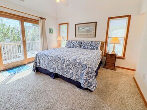 A bedroom with a large bed, a wooden nightstand, a window with blinds, and a door leading to a balcony. - House N Duck - Located in the heart of Duck, this 5 BR home is a pleasant walk away from the beach! (Duck)