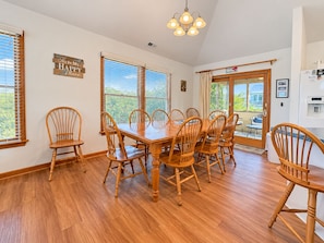 A dining room with a wooden table and chairs, large windows, and a view of the outdoors. - House N Duck - Located in the heart of Duck, this 5 BR home is a pleasant walk away from the beach! (Duck)