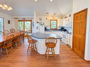 A modern kitchen with a central island, wooden chairs, and a dining table. - House N Duck - Located in the heart of Duck, this 5 BR home is a pleasant walk away from the beach! (Duck)