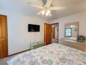 Ein Schlafzimmer mit einem Bett, einem Deckenventilator, einem Fernseher, einem Schminktisch und einem Spiegel.