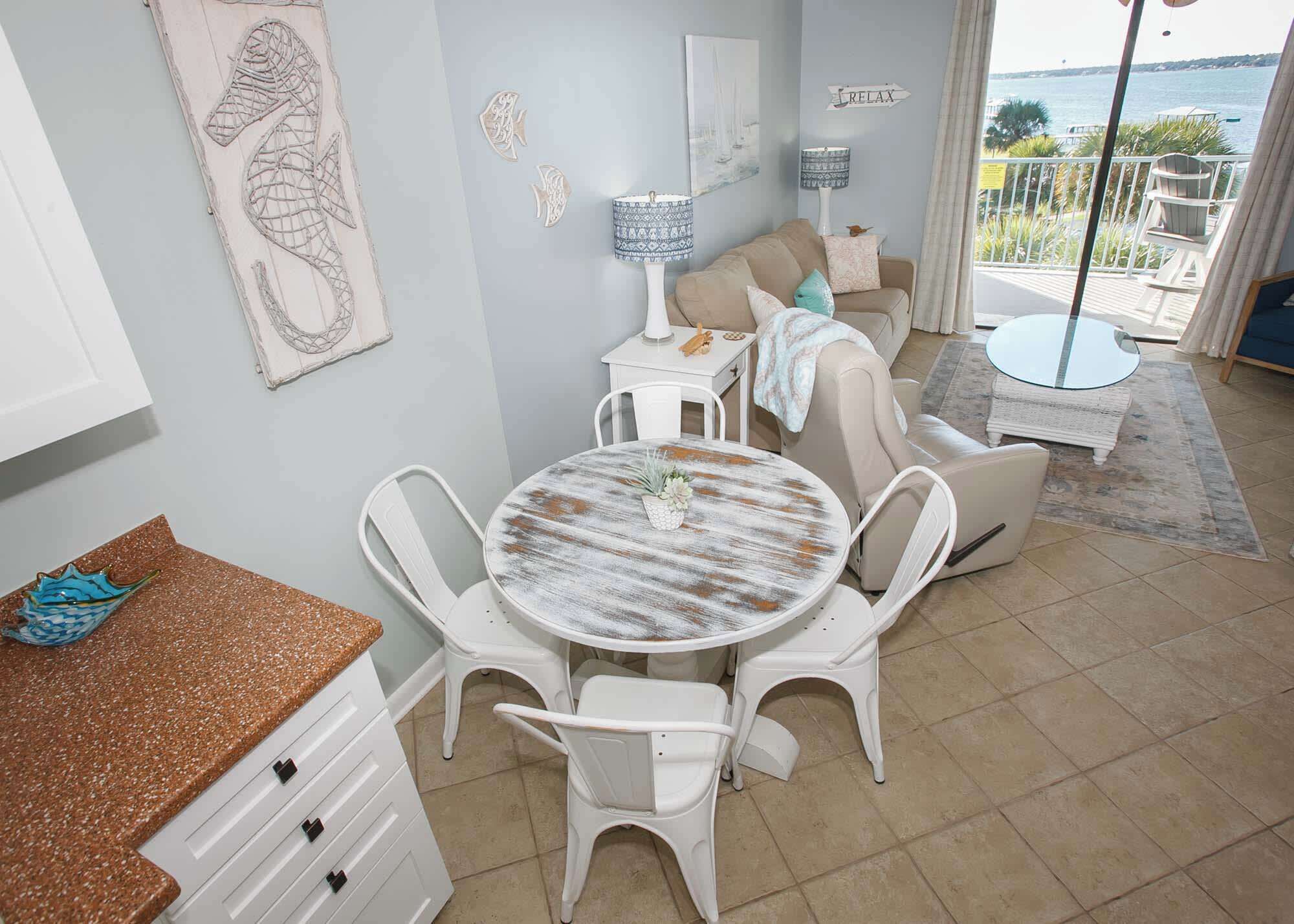 A dining area with a round table, white chairs, and a view of the sea through large windows.