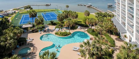 A resort with a swimming pool, tennis courts, and a view of the water.