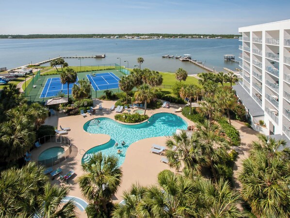 A resort with a swimming pool, tennis courts, and a view of the water.