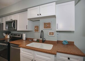 A kitchen with white cabinets, a granite countertop, a stainless steel microwave, a sink, and decorative wall art.