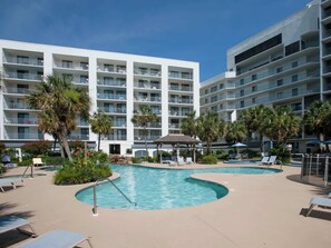 Ein Hotel mit mehreren Balkonen, einem Poolbereich mit Liegestühlen und Palmen.