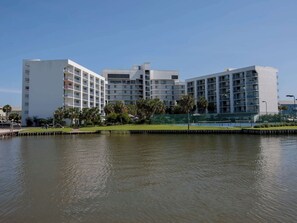A modern hotel with multiple floors, a waterfront view, and a well-maintained lawn area.