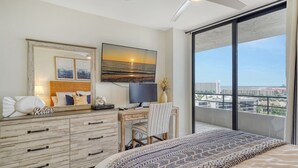 A bedroom with a bed, a desk, a TV, and a large window with a city view. - Anchorage PH-2 in Siesta Key, FL (Siesta Key)