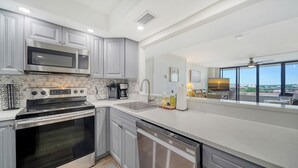 A modern kitchen with stainless steel appliances, a dishwasher, and a large window offering a city view. - Anchorage PH-2 in Siesta Key, FL (Siesta Key)