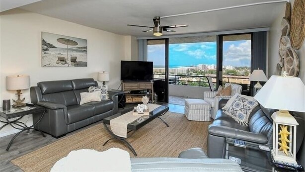 A modern living room with a black leather sofa, a flat-screen TV, a coffee table, and a balcony with a city view. - Anchorage PH-2 in Siesta Key, FL (Siesta Key)