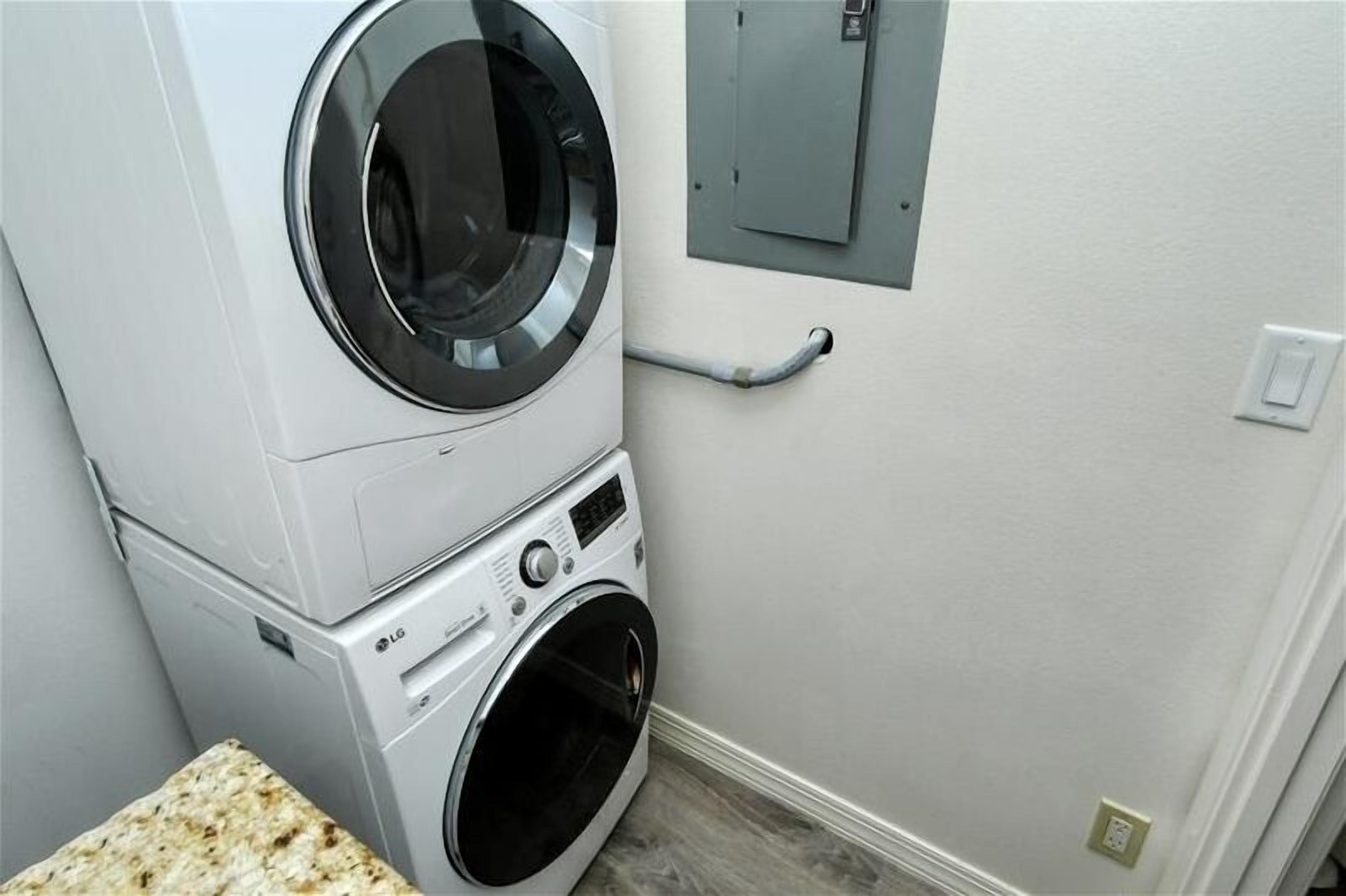 Une buanderie équipée d’une machine à laver et d’un sèche-linge superposés, d’une boîte de raccordement métallique et d’une main courante.