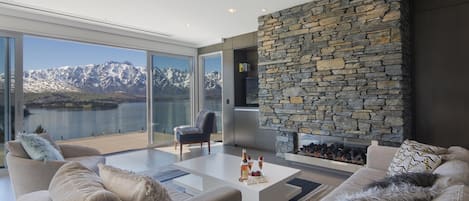 Una sala de estar moderna con chimenea de piedra, ventanas amplias que ofrecen vistas a la montaña y un rincón de estar acogedor.