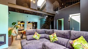 Un salon moderne avec un canapé d’angle gris, un coin repas et un escalier menant à un niveau supérieur.
