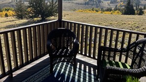 A wooden deck with two wicker chairs, overlooking a hilly landscape with autumn foliage.