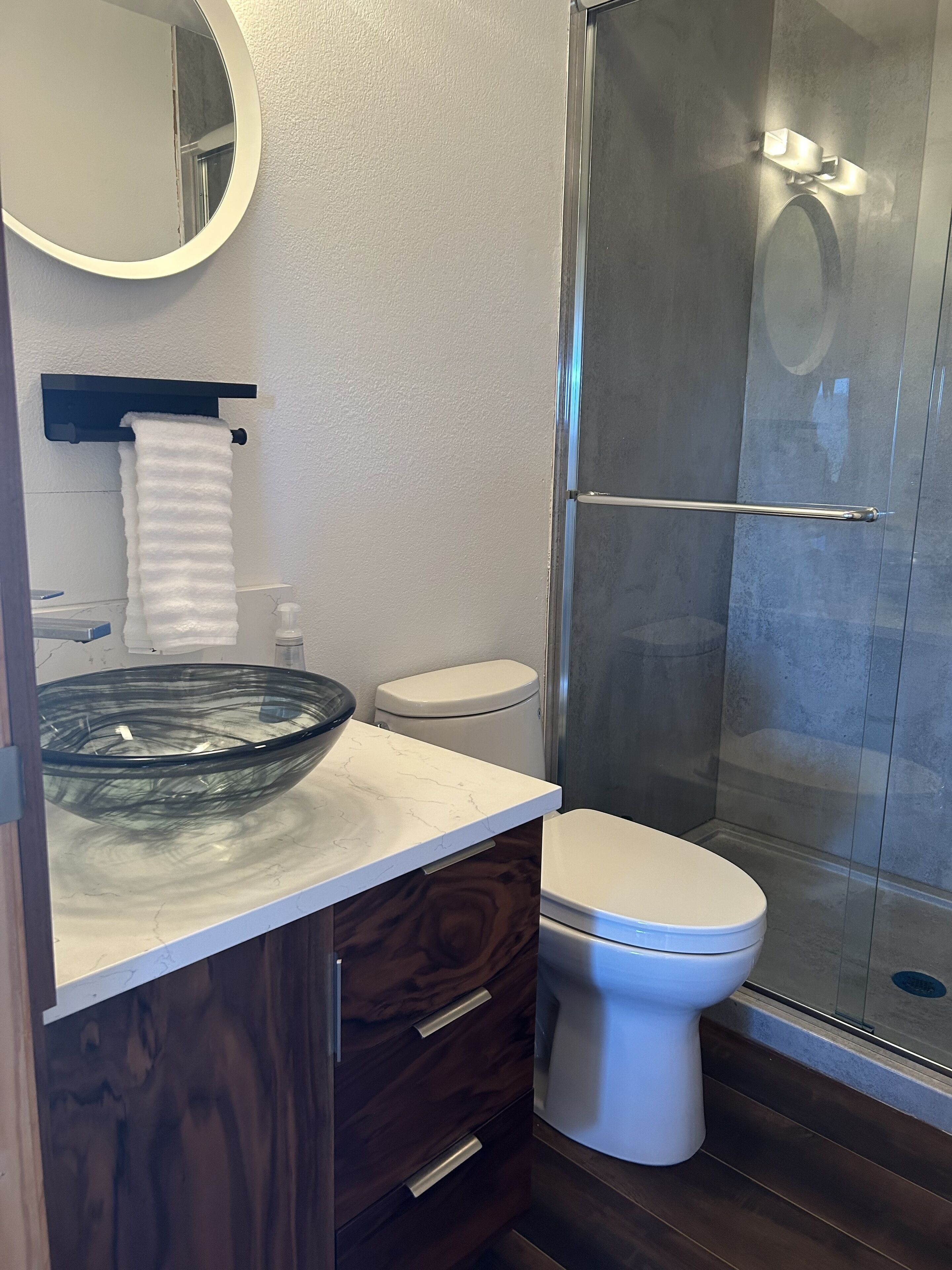 Une salle de bain moderne avec un lavabo en forme de bol en verre, des toilettes blanches et une douche à parois de verre.