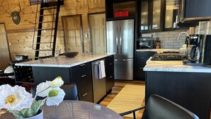 A modern kitchen with a central island, stainless steel appliances, and a wooden wall with a mounted deer head.