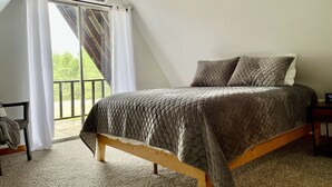 Ein Schlafzimmer mit Bett, Nachttisch, Stuhl und Blick ins Freie durch ein Fenster mit Vorhängen.